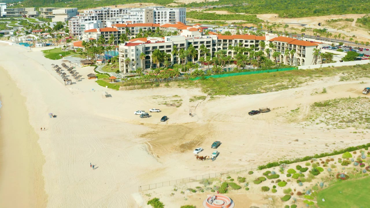 Closer aerial angle on the resort with umbrellas along the beach and ocean at left.