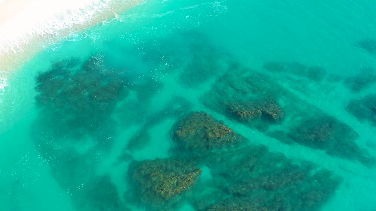Turquoise shallows with submerged rocks and surf at the beach edge.