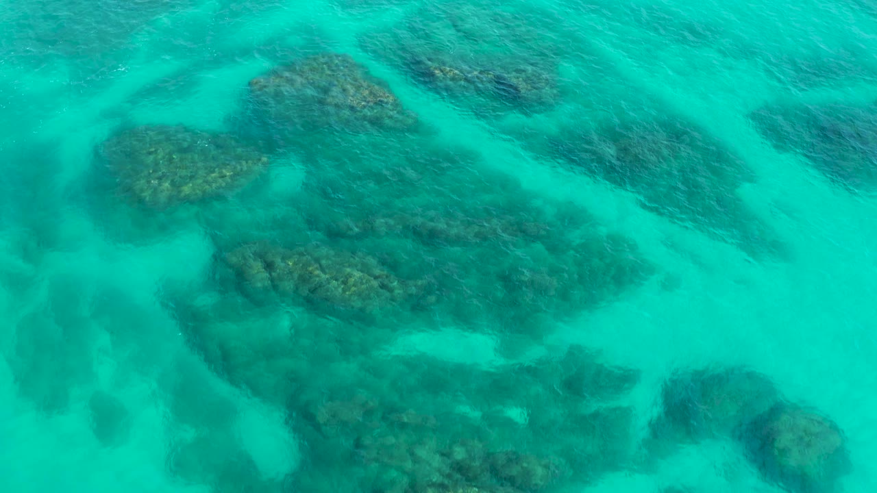 Straight-down frame of shallow reef shapes under blue-green ocean water in Baja California Sur, with faint surface texture and no visible people.
