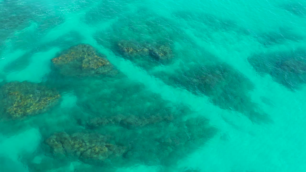 Aerial view in Baja California Sur with several reef formations separated by pale sandy channels in turquoise water, with no visible people.