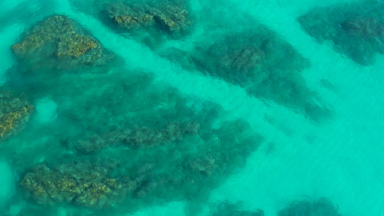Aerial overhead frame shows larger dark reef masses under clear turquoise water in Desert Park Natural Reserve, Baja California Sur, with no visible people.