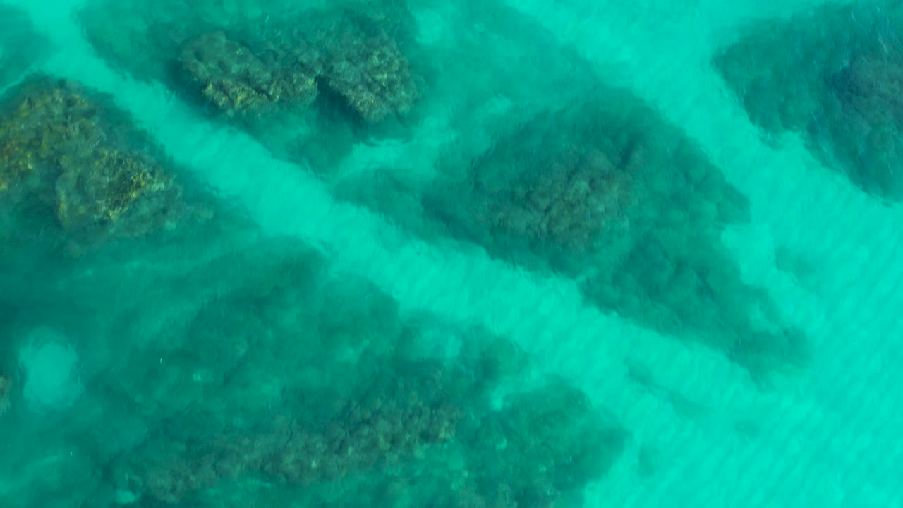 Top-down turquoise water with dark reef shapes below the surface.