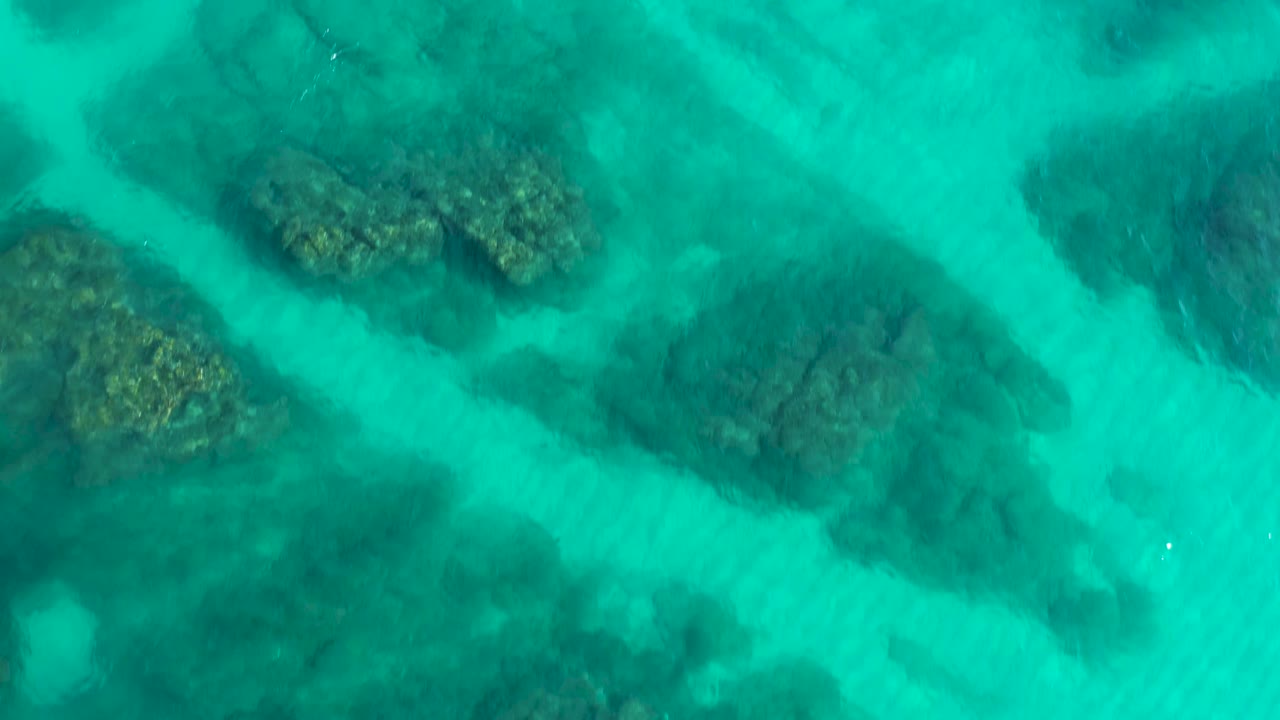 Top-down aerial frame with diagonal reef formations visible through turquoise sea at Desert Park Natural Reserve, Baja California Sur, Mexico, with no visible people.