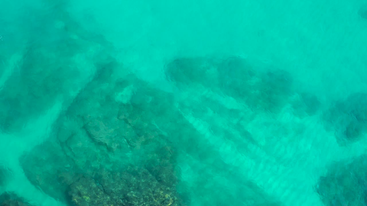 Aerial frame from the Mexico reserve with submerged rocky patches, branching sandy channels, light surface texture, and no visible people in the water.