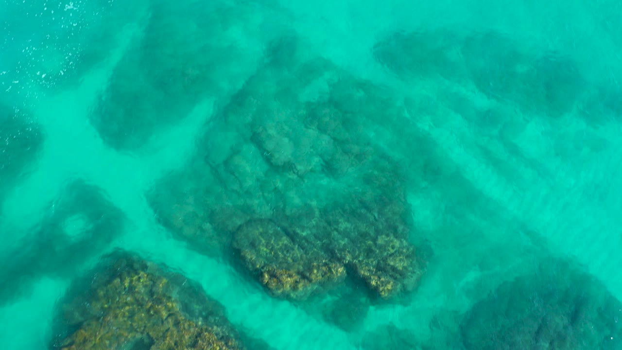 Overhead view in Desert Park Natural Reserve, Baja California Sur, showing turquoise shallow water, clustered submerged rocks, pale sand channels, and no visible people.