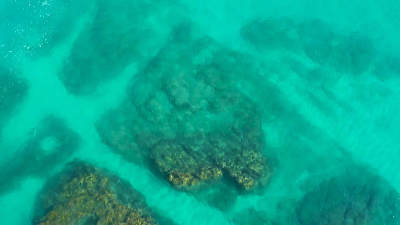 A second overhead frame from Desert Park Natural Reserve shows teal water revealing a broad central rock formation, lighter sand streaks, and no visible people.