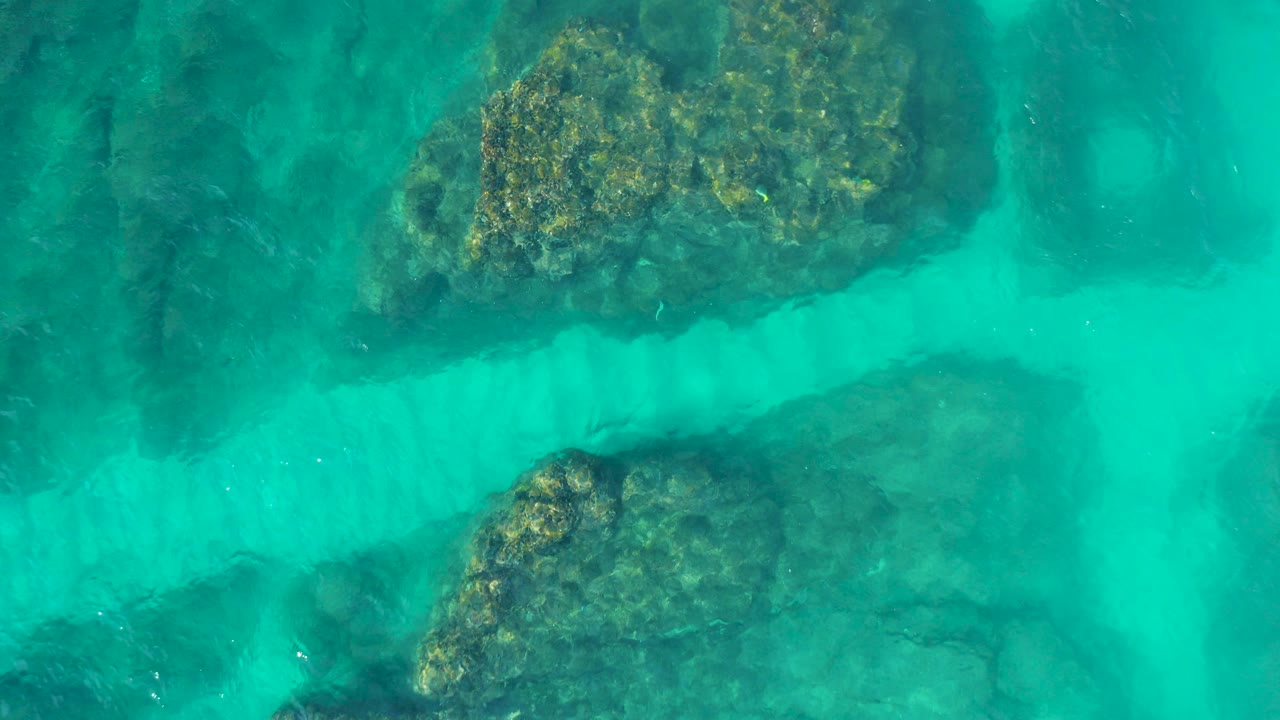 Opening overhead frame from Desert Park Natural Reserve shows turquoise water, pale sandy channels, and submerged brown-green rocks with no visible people.