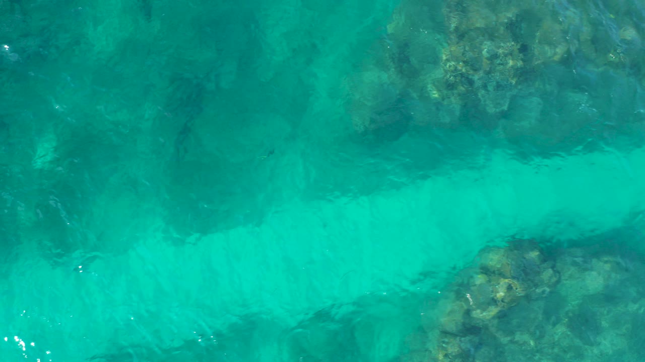 Top-down view of turquoise water over submerged reef or rocky seabed at Desert Park Natural Reserve in Baja California Sur, Mexico, with no visible people.