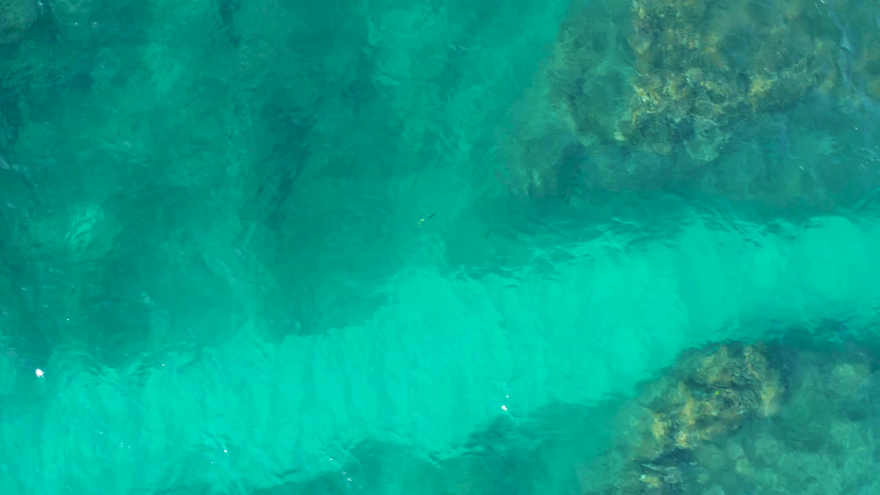 Aerial top-down frame of turquoise sea above scattered rocky reef formations at Desert Park Natural Reserve, with no visible people or vessels.