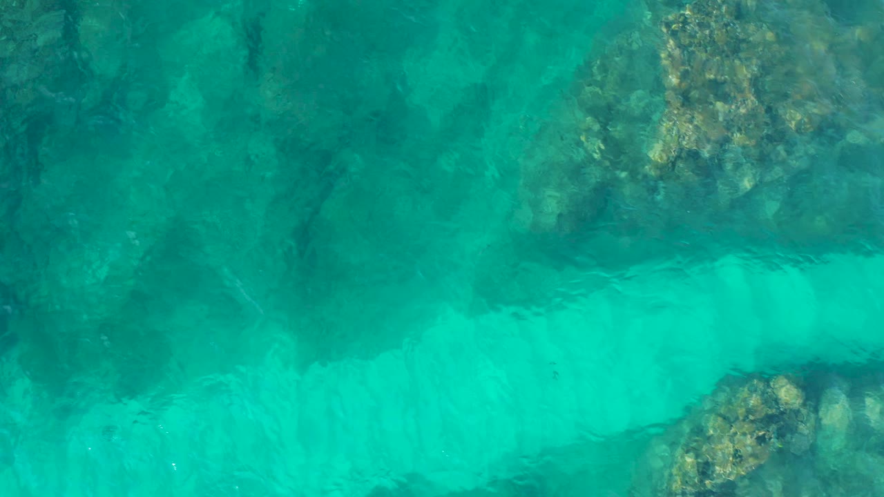Large submerged reef patch sits under green-blue water in Baja California Sur, Mexico, with soft ripples across the surface and no visible people.