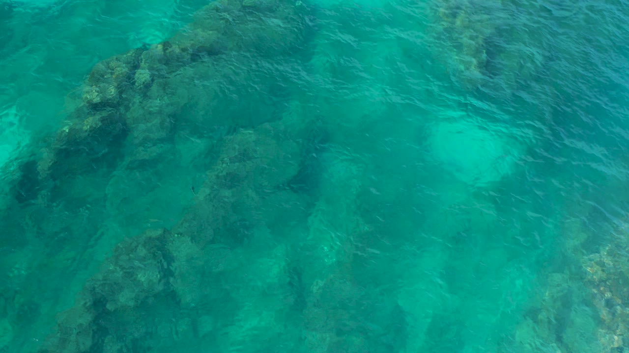 Top-down aerial view of turquoise water over dark submerged rocks in Desert Park Natural Reserve, Baja California Sur, with no visible people.