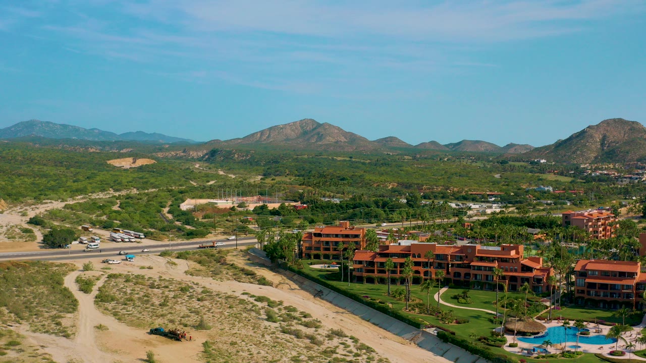 Aerial view of terracotta resort buildings, pool, desert scrub, highway, and mountains.