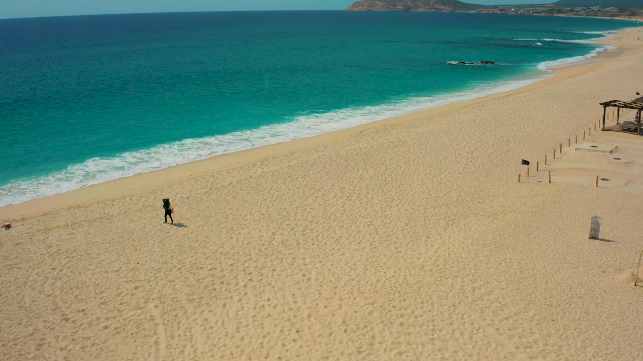 Wide sandy beach with a lone walker and diagonal shoreline.