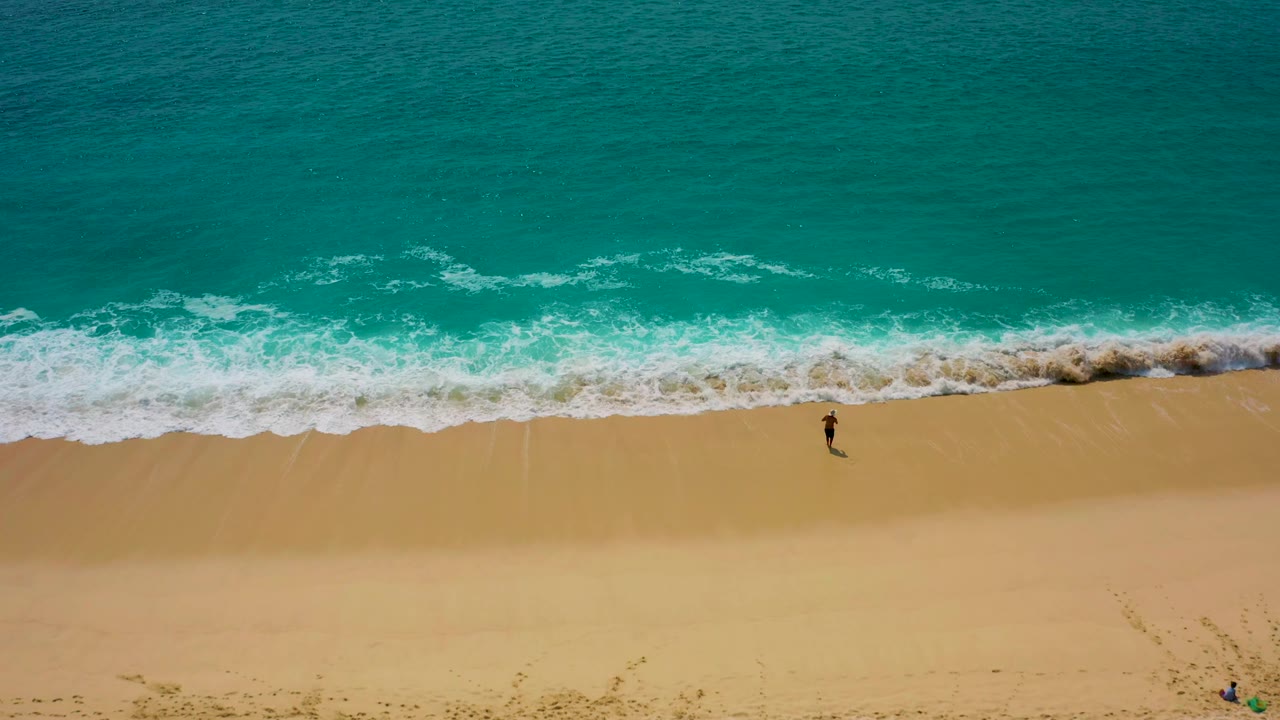 High drone view in Desert Park Natural Reserve, Baja California Sur, showing the surfer near the lower surf edge while a wider turquoise wave line curls toward shore.