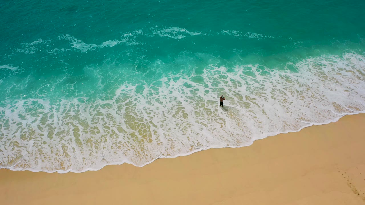 Surfer remains in shallow surf as a wide band of foam reaches the sand.