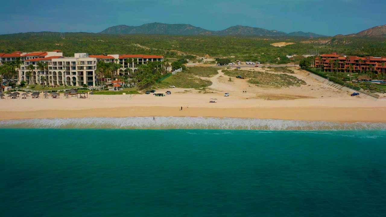 Aerial coastline view with resort complexes behind a sandy beach and turquoise water.