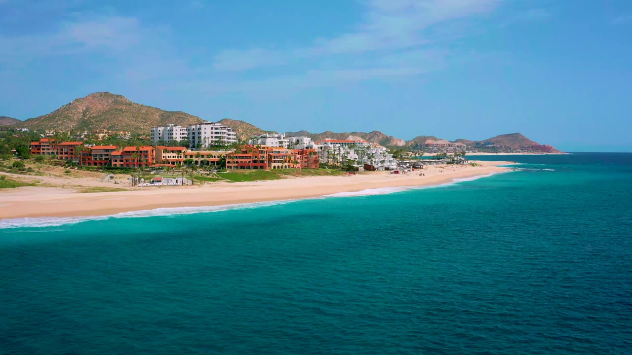 Coastal resort buildings beside a wide beach and bright turquoise water.