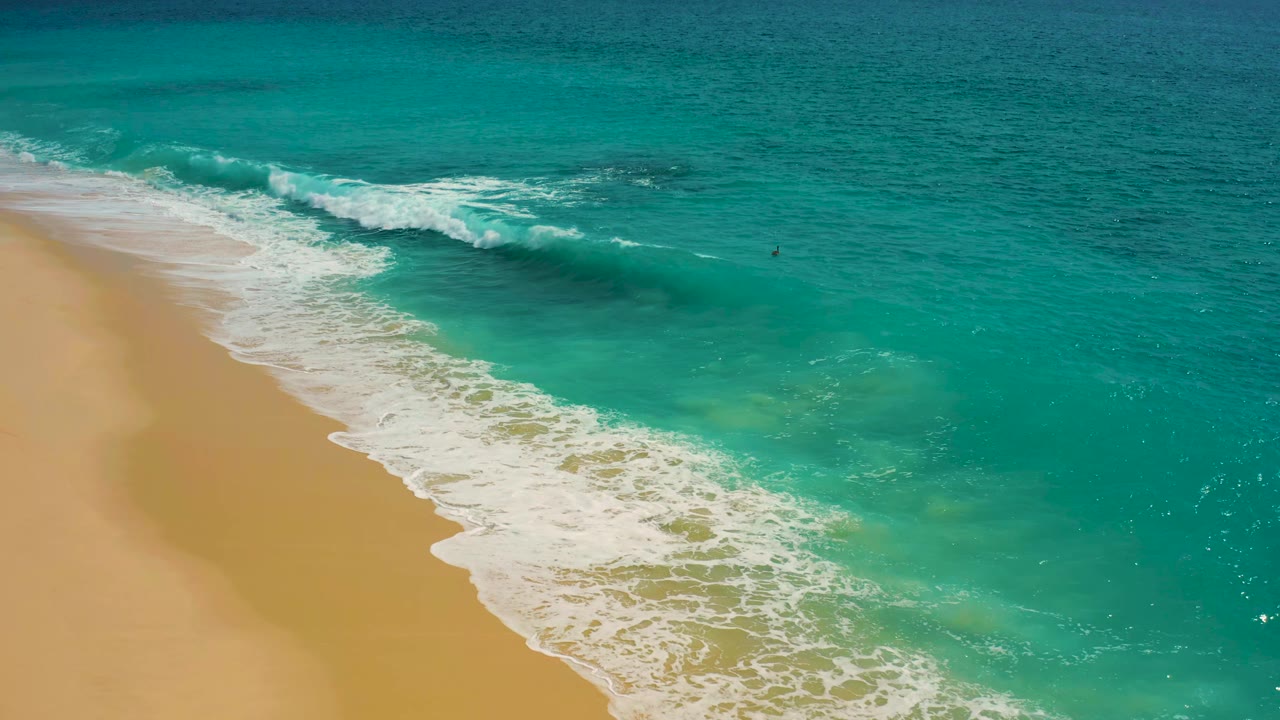 Aerial view over Desert Park Natural Reserve with a broad white wave line curling across aquamarine shallows and tan sand along the left side.