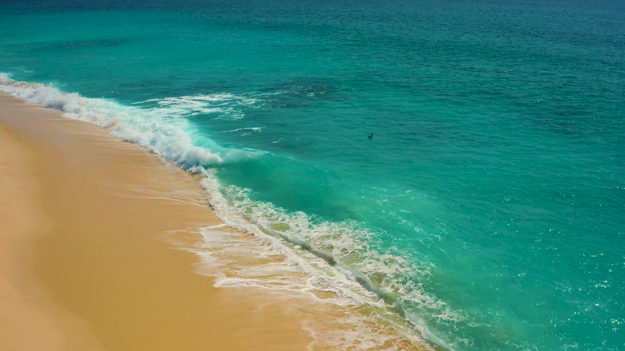 White surf spreading across clear turquoise water and sand.