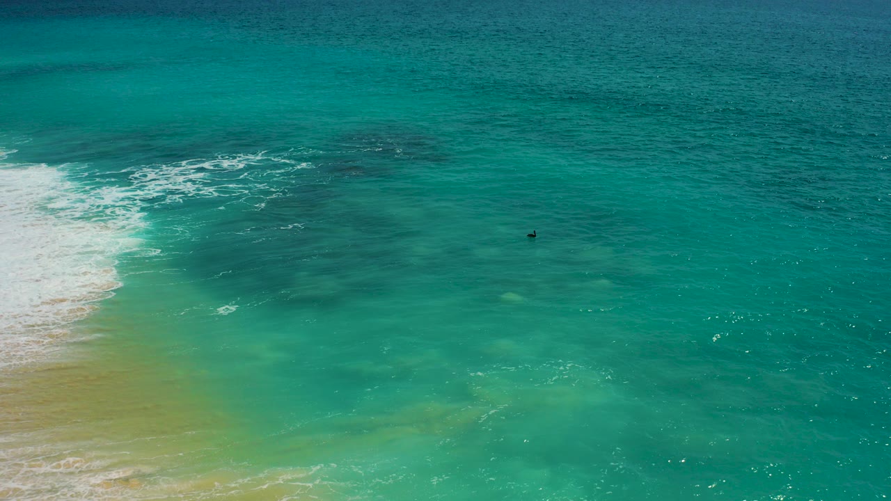 Turquoise ocean with white surf reaching a sandy shoreline.