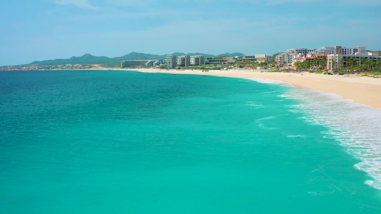 Aerial beach view with blue-green ocean, white breakers, and coastal buildings