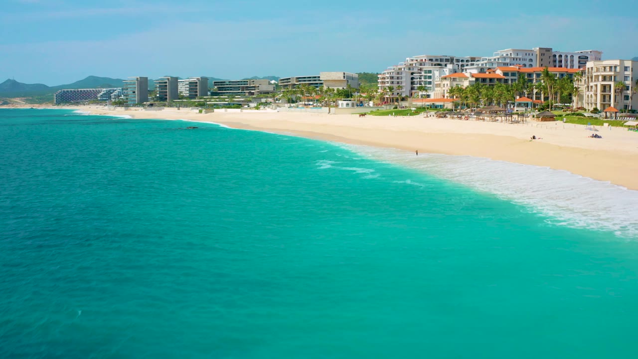 Aerial view along Desert Park Natural Reserve shoreline, where turquoise ocean meets a long pale beach and multi-story coastal hotels stand behind a row of palms.