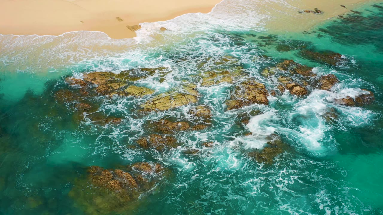 Foamy waves spreading over shallow rocks near sand