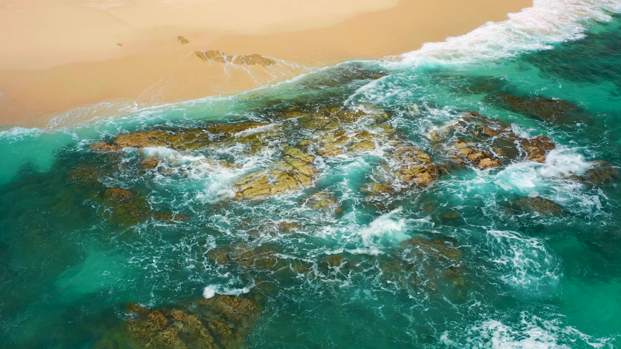Turquoise surf washing over rocks beside a sandy beach