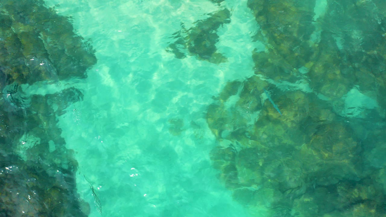 Top-down aerial view of turquoise shallow water over dark submerged rocks in Baja California Sur, Mexico, with no visible people.
