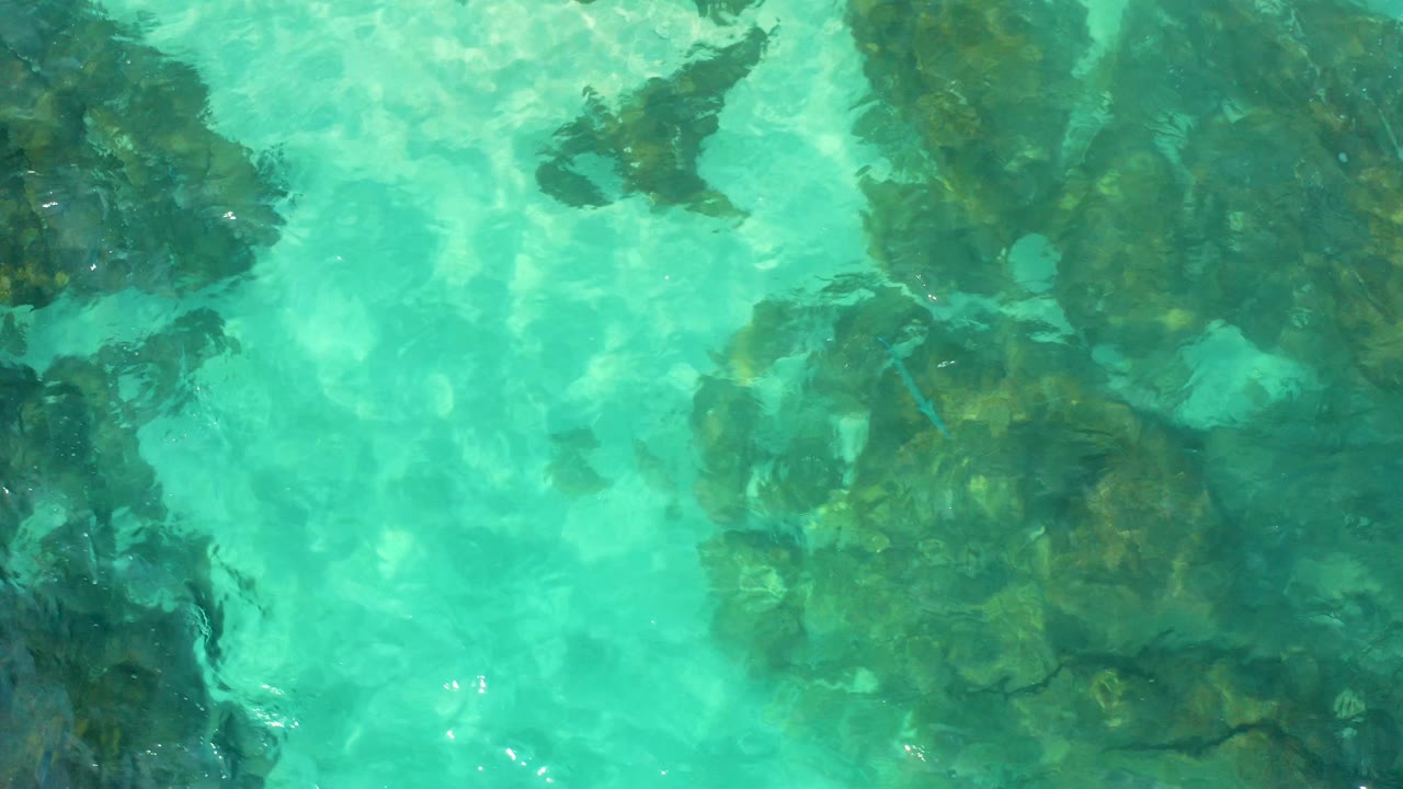 Aerial top-down view of bright turquoise shallows over darker submerged rock masses in Baja California Sur, Mexico, with no visible people.