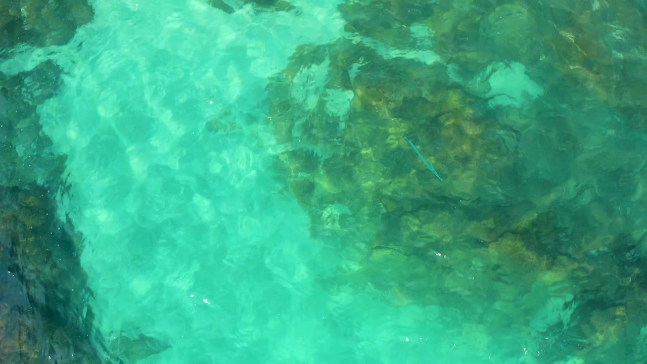 Aqua water fills the frame above a darker rock patch, with rippled surface light and no visible people in Baja California Sur, Mexico.