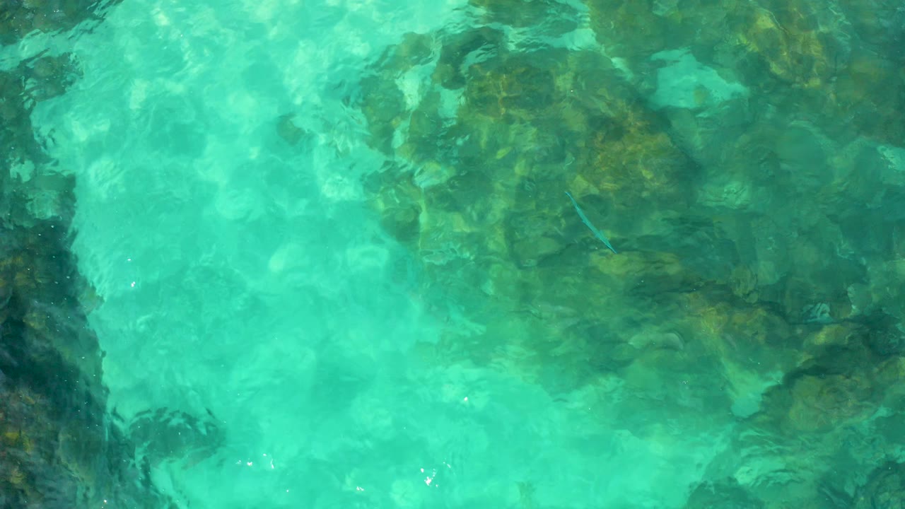 Shallow turquoise sea covers an uneven dark rock formation, with soft wave distortion and no visible people in Baja California Sur, Mexico.