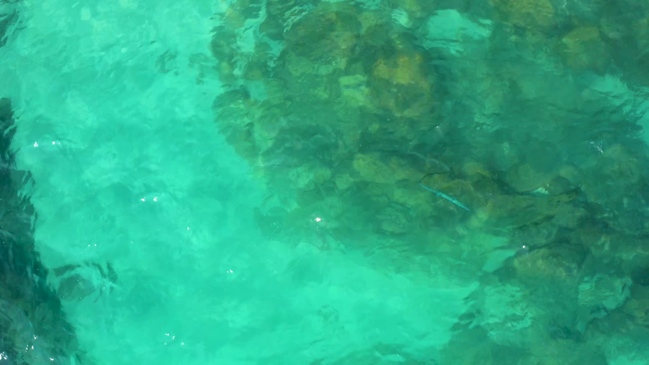 Clear teal water covers a clustered rocky seabed in Baja California Sur, with gentle wave distortion and no visible people.