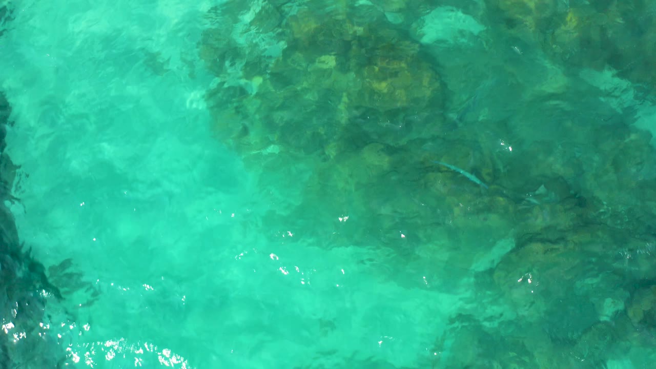 Turquoise water ripples over reef-like dark rock formations in Baja California Sur, with small bright glints and no visible people.