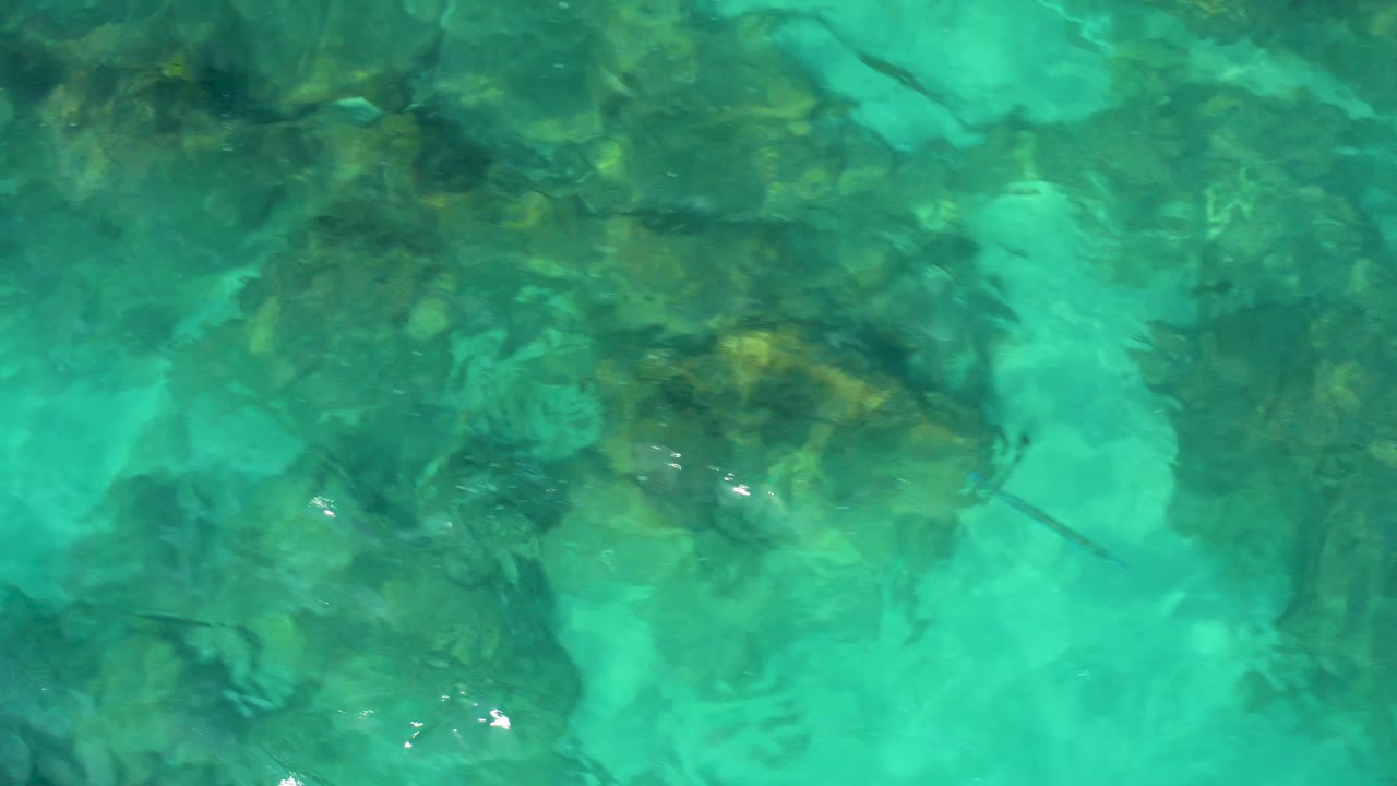 Direct overhead frame from Desert Park Natural Reserve showing rippled turquoise water over a broad dark boulder patch, with no visible people.