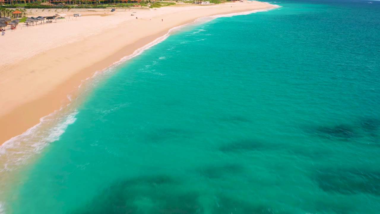 High-angle frame at Desert Park Natural Reserve in Baja California Sur, Mexico, with broad turquoise ocean filling most of the view, pale sand at the top, scattered darker underwater patches, and no visible people.