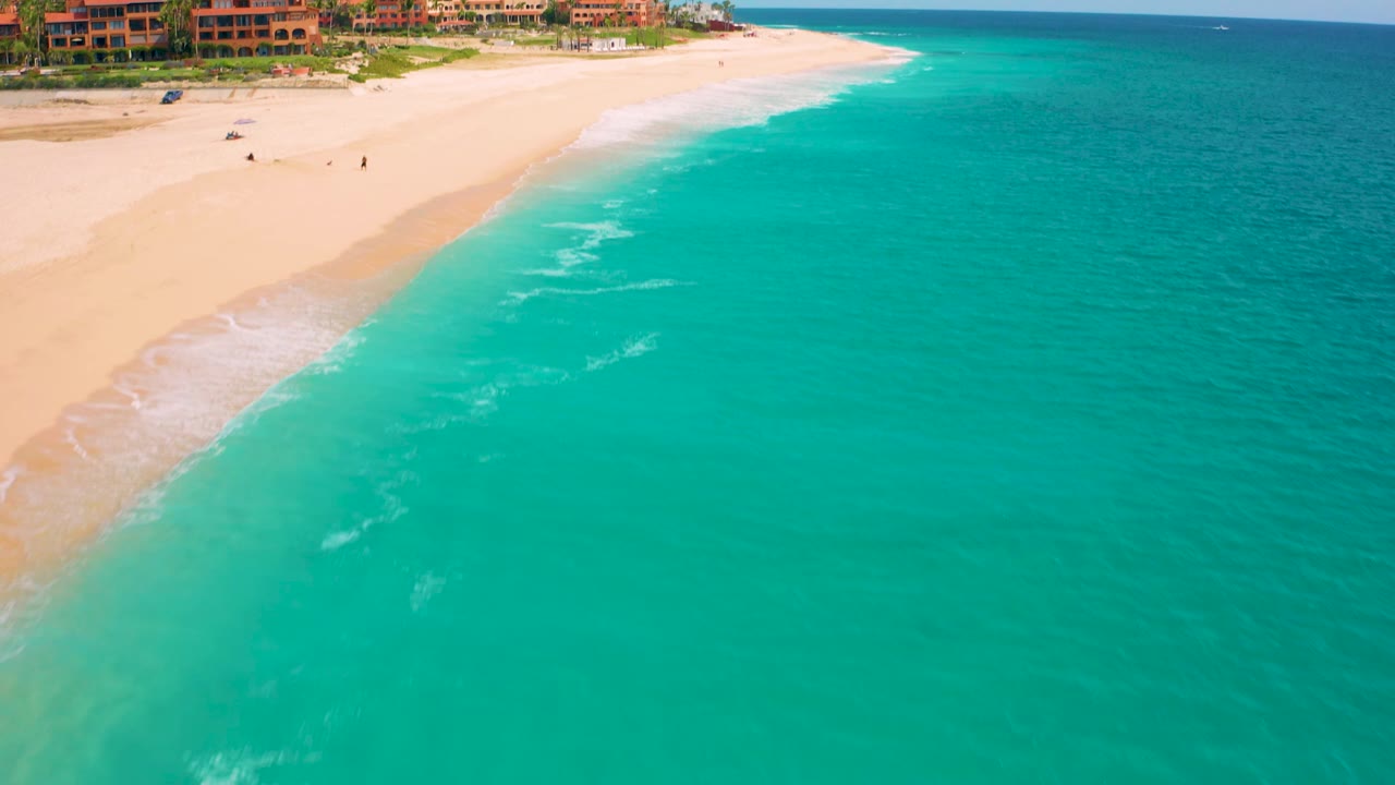 Aerial beach shoreline with turquoise water and resort buildings.