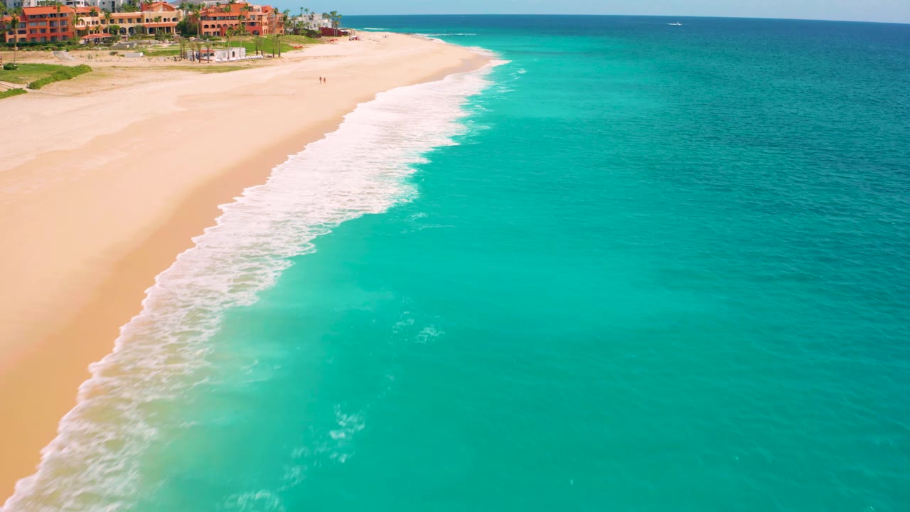 Diagonal shoreline with white waves rolling onto sand beside clear turquoise water.