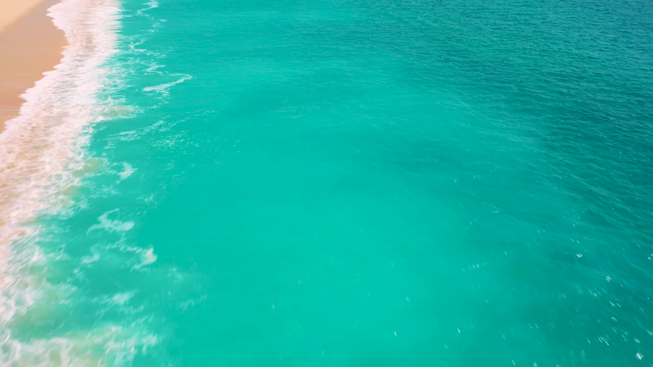 Aerial turquoise ocean beside a sandy shoreline