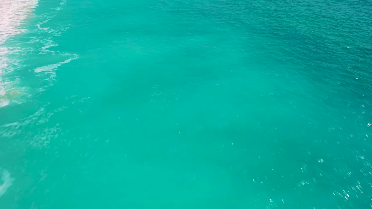 High-angle Baja California Sur ocean view with the surf line mostly cropped to the far left and uninterrupted turquoise water across the center, with no visible people.