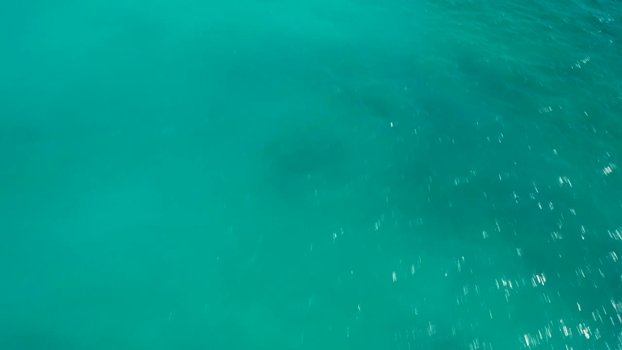 High-angle view of teal ocean surface in Baja California Sur, Mexico, where small white sun glints appear across the right side and no visible people are present.