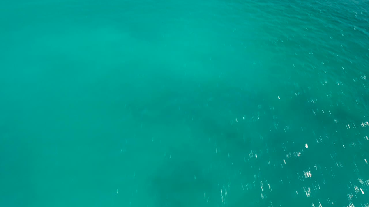 Overhead ocean surface in Baja California Sur, Mexico, with turquoise water, faint shadowy patches, brighter ripple highlights toward the lower right, and no visible people.