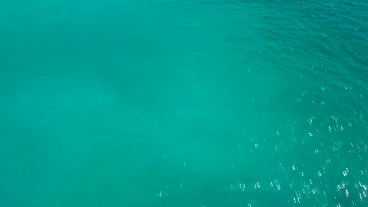 Smooth teal ocean surface with small ripples and darker green-blue patches