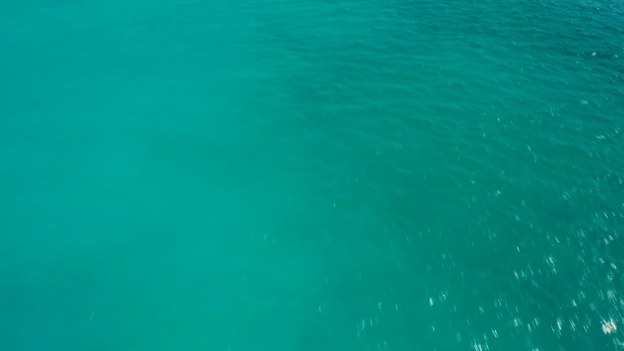 Opening aerial frame over turquoise ocean water in Desert Park Natural Reserve, Baja California Sur, Mexico, with faint ripples and no visible people.