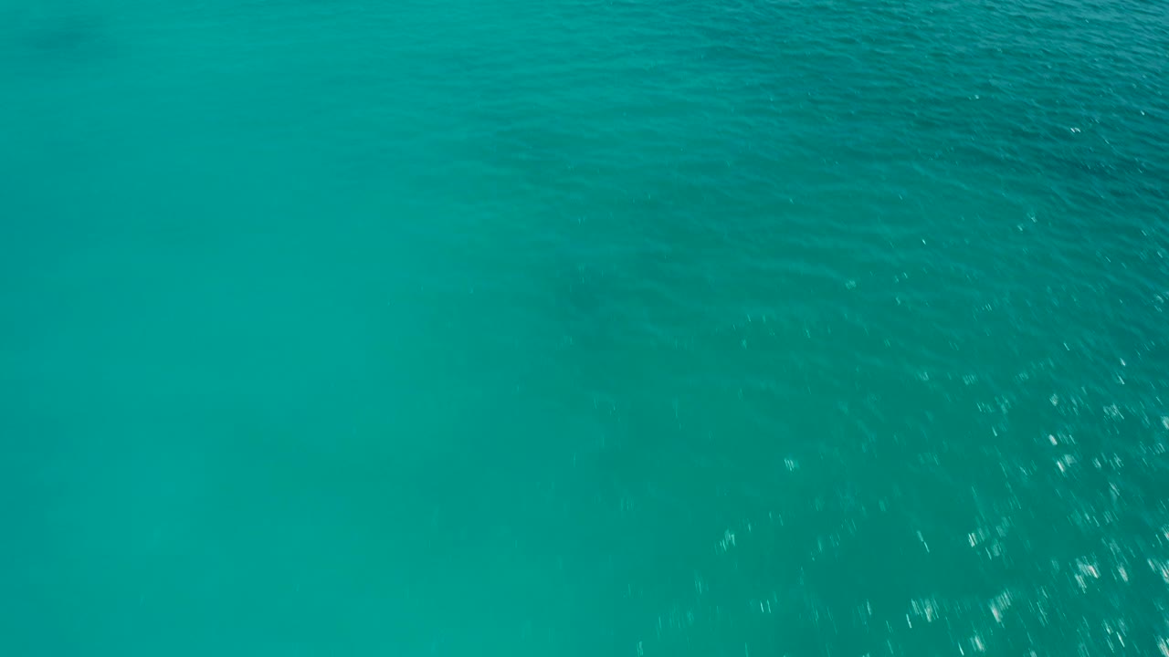 Downward aerial frame of open turquoise sea in Baja California Sur, Mexico, with darker teal patches and no land, boats, or visible people.