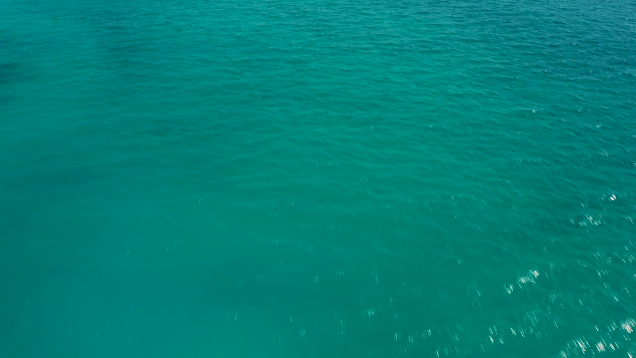 High aerial view of turquoise ocean water in Baja California Sur, Mexico, with soft ripples, faint darker patches below the surface, and no visible people.