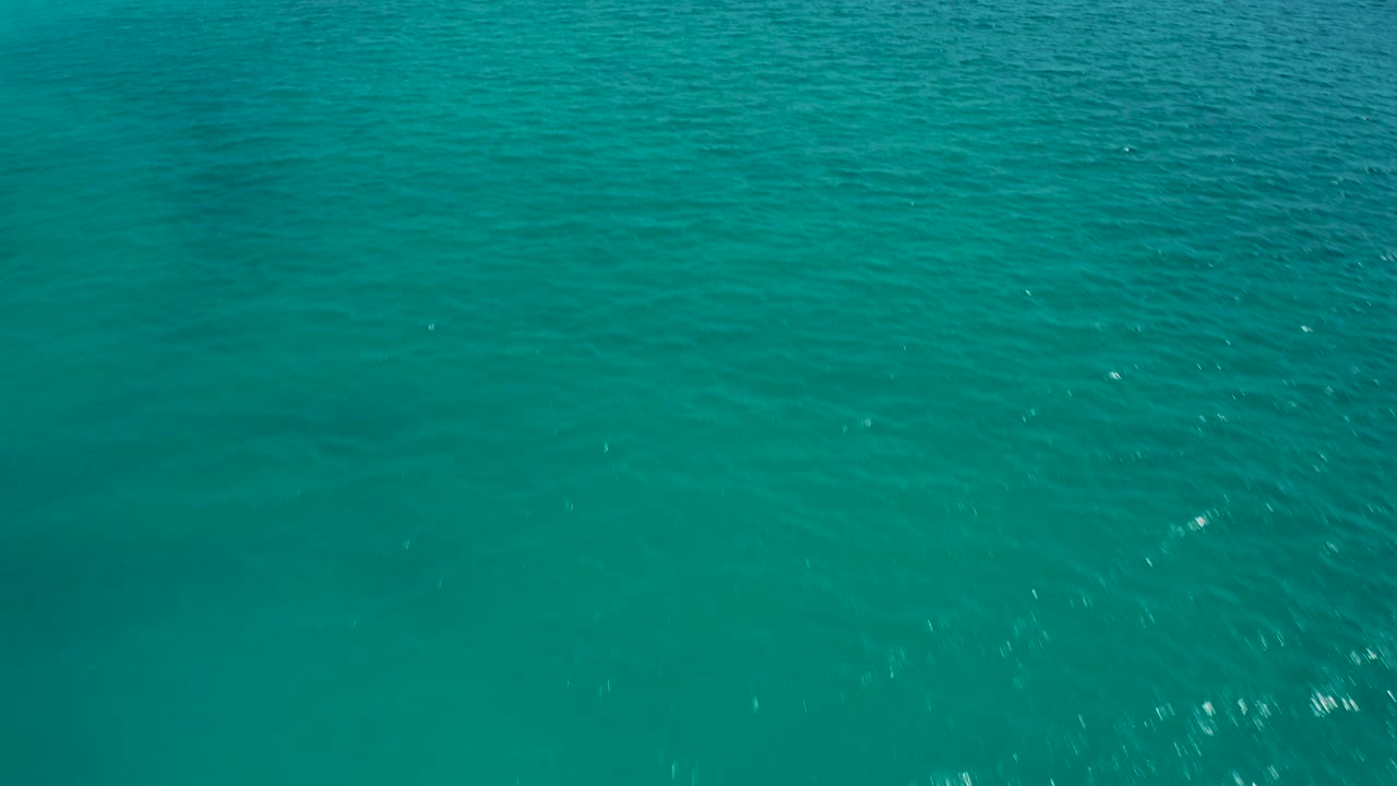 Drone-height view of open turquoise ocean in Baja California Sur, Mexico, with fine wave lines, small white reflections, and no visible people.