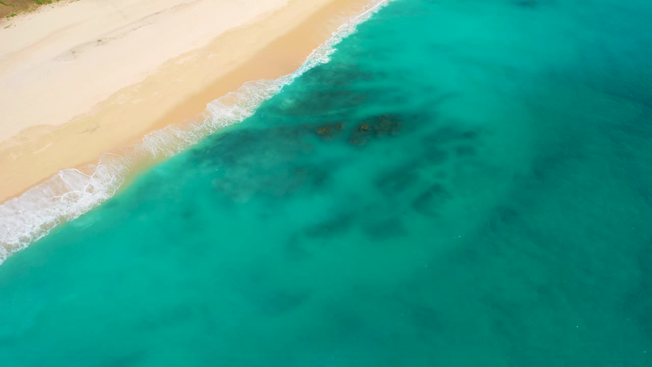 Overhead turquoise water beside a sandy beach with small white surf.