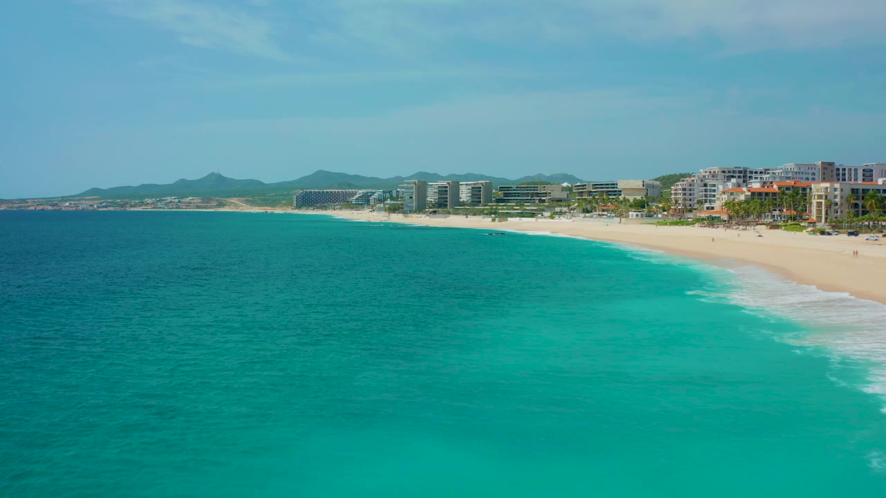 Aerial view of a curved beach with turquoise water and buildings inland.