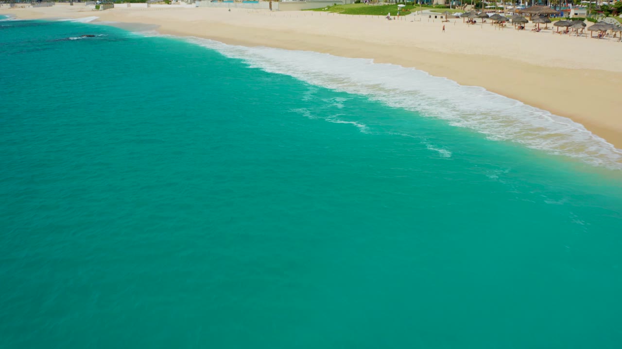 High-angle view of turquoise water meeting sandy beach in Baja California Sur, with white foam near the shore and no visible people.
